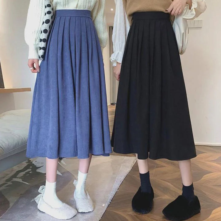 Zwei Frauen in blauen und schwarzen Faltenröcken, modische Winterkleidung, Innenraum.