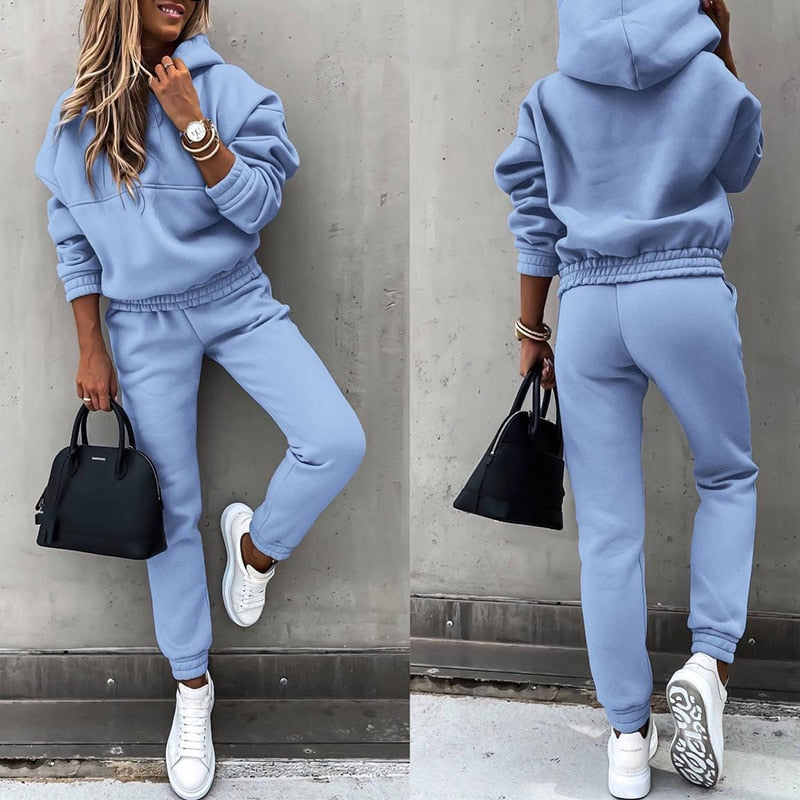 Frau in hellblauem Jogginganzug, weiße Sneaker, schwarze Handtasche, lässiger Stil.