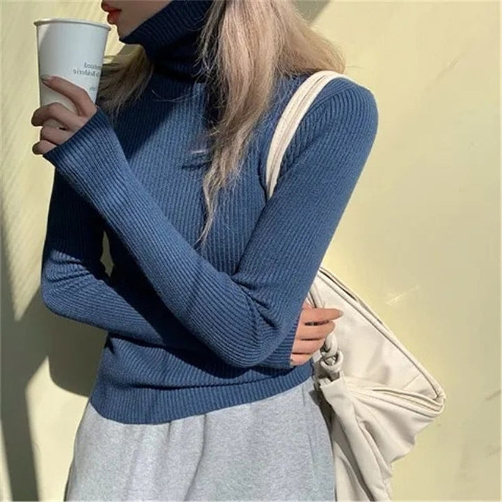 Frau in blauem Rollkragenpullover mit Kaffeebecher und weißer Tasche vor gelbem Hintergrund.