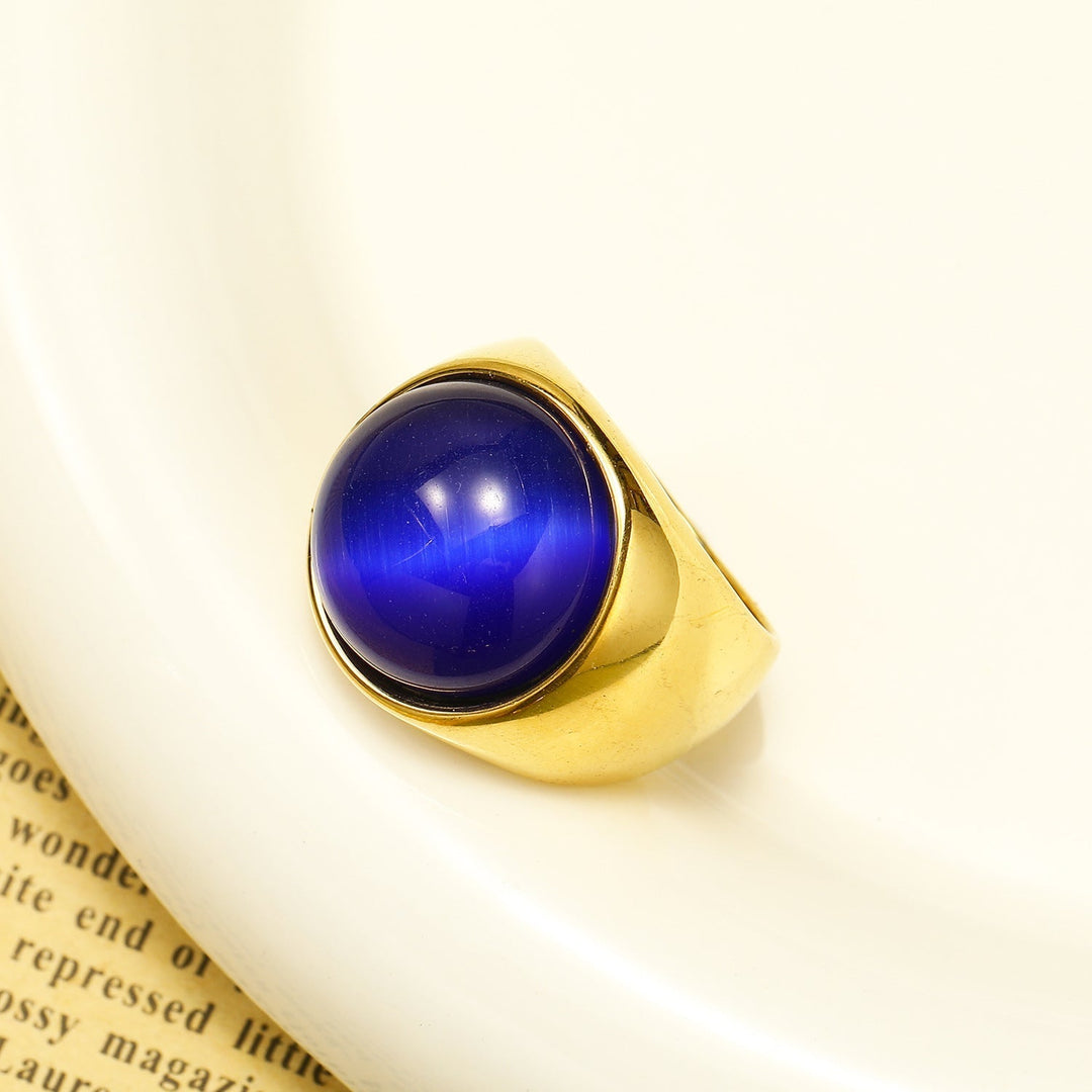Goldener Ring mit großem, rundem blauen Edelstein auf weißem Hintergrund.