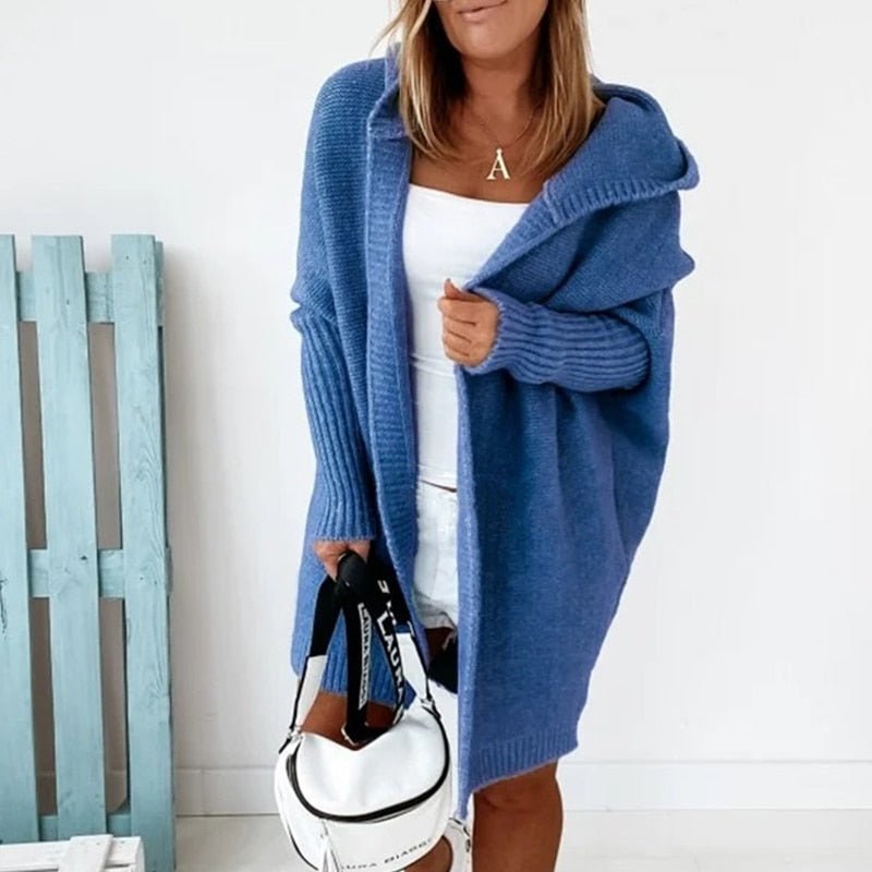 Frau trägt blauen Strick-Cardigan mit Kapuze, hält weiße Tasche, modisch, gemütlich.