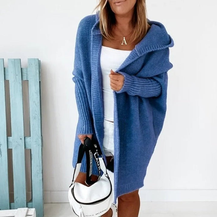 Frau in blauem Strick-Cardigan mit Kapuze, hält weiße Tasche, modisch, gemütlich.