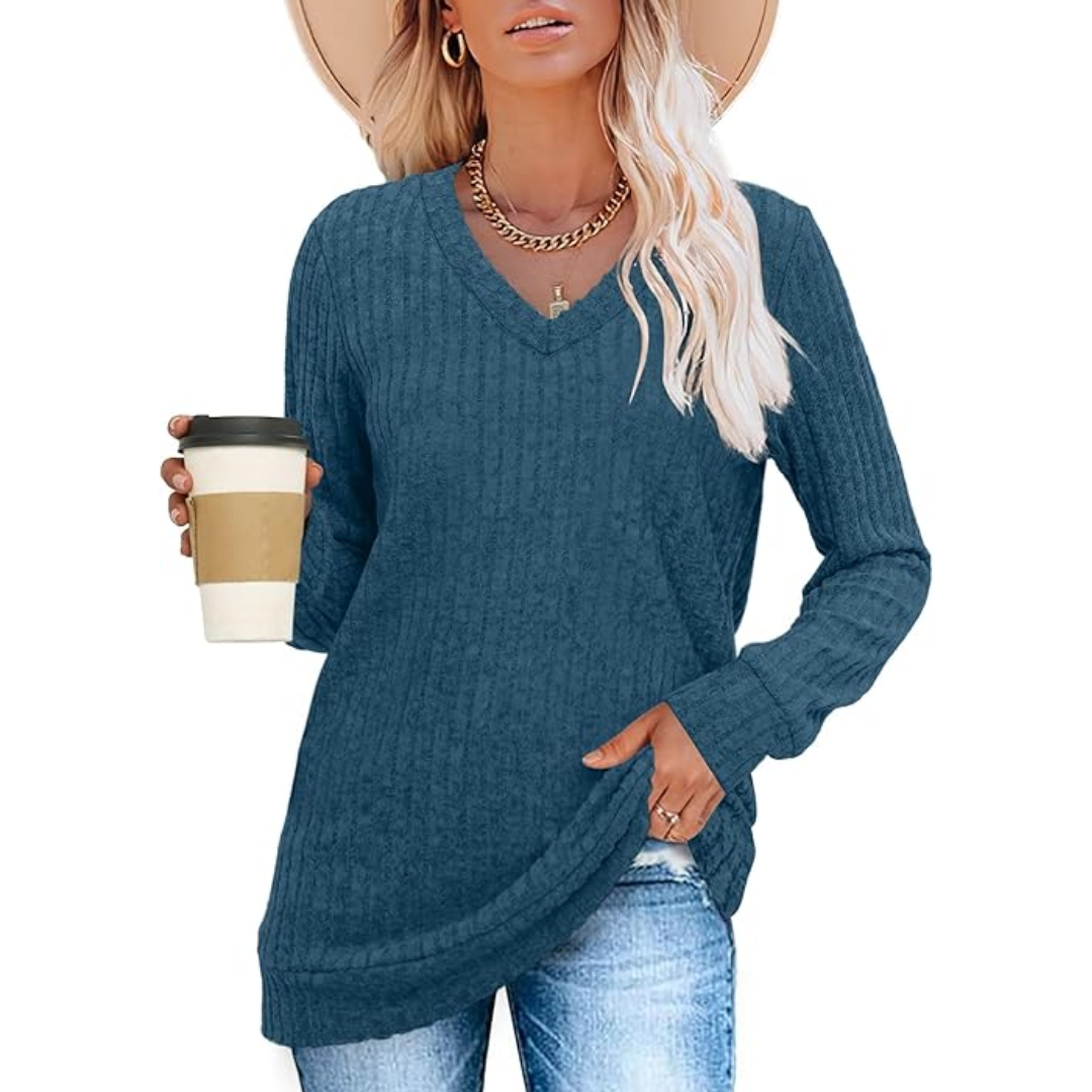 Frau in blauem V-Ausschnitt-Pullover, hält Kaffeebecher, trägt Hut und Jeans.