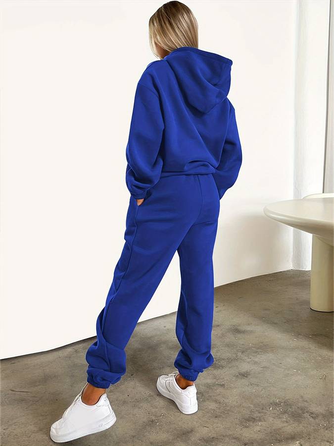 Frau in blauem Hoodie und Jogginghose, weiße Sneaker, lässige Mode, Streetwear-Outfit.