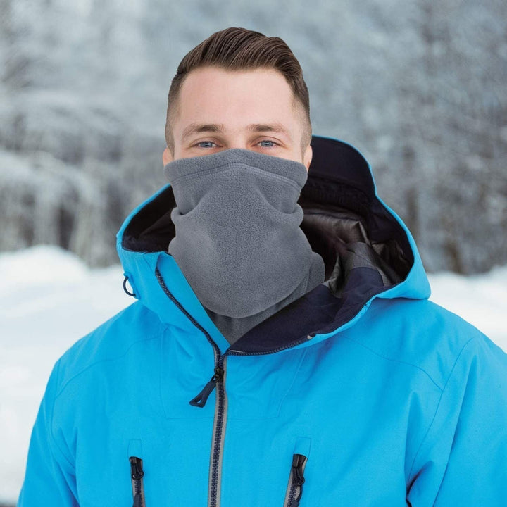 Mann in blauer Winterjacke mit grauem Fleece-Schal im verschneiten Wald.