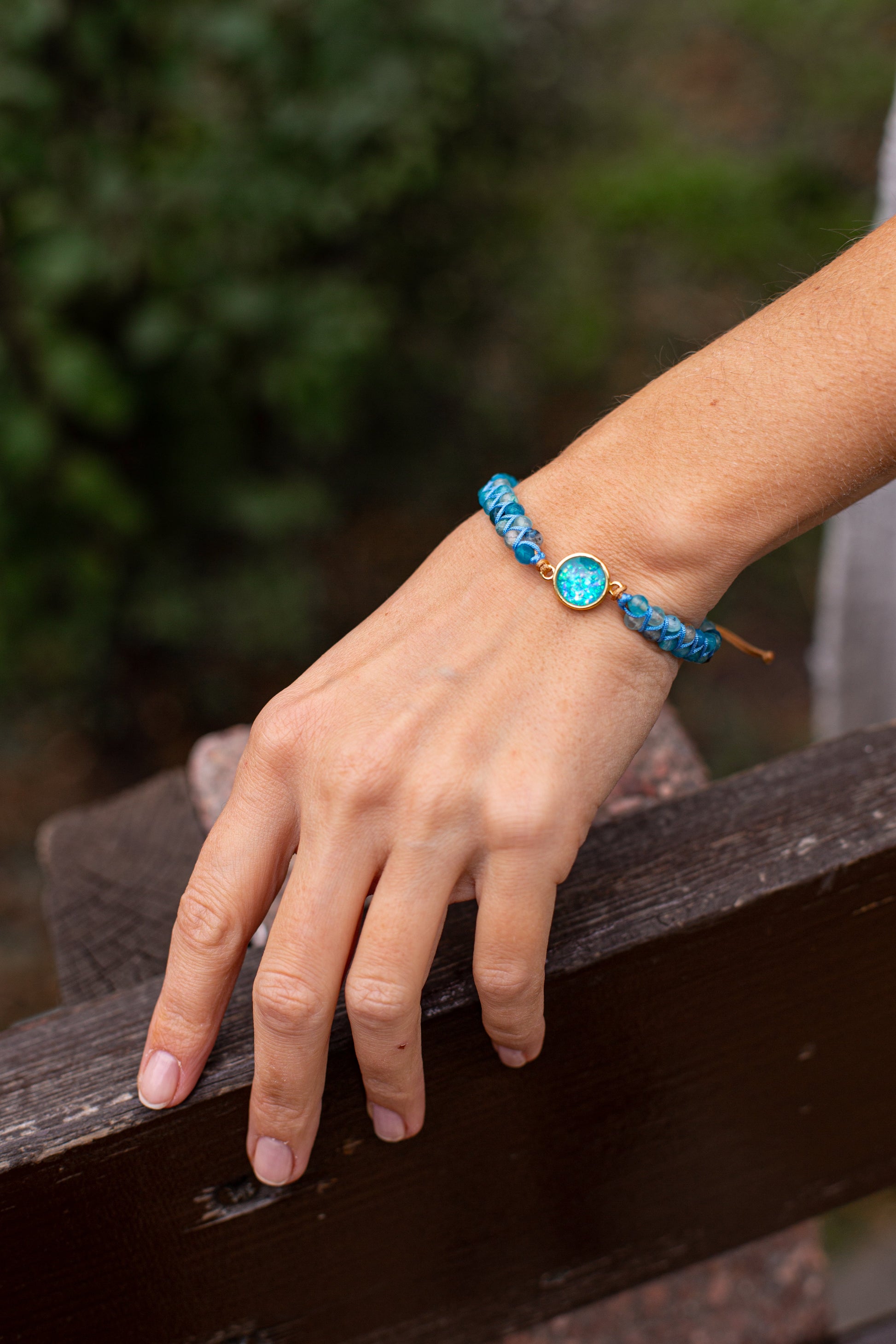 Hand mit blauem Armband aus Perlen und Kristall auf Holzbank, Schmuck, Modeaccessoire.
