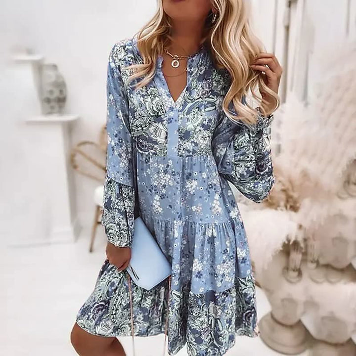 Frau in geblümtem blauen Kleid mit langen Ärmeln, hält hellblaue Tasche, modisch, elegant.