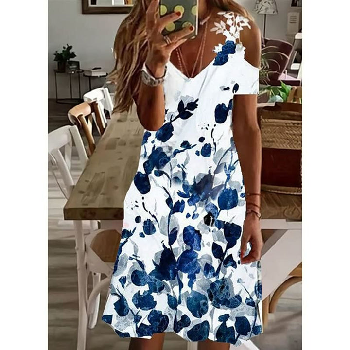 Frau in weißem Sommerkleid mit blauen Blumenmuster, V-Ausschnitt, schulterfrei, im Esszimmer.