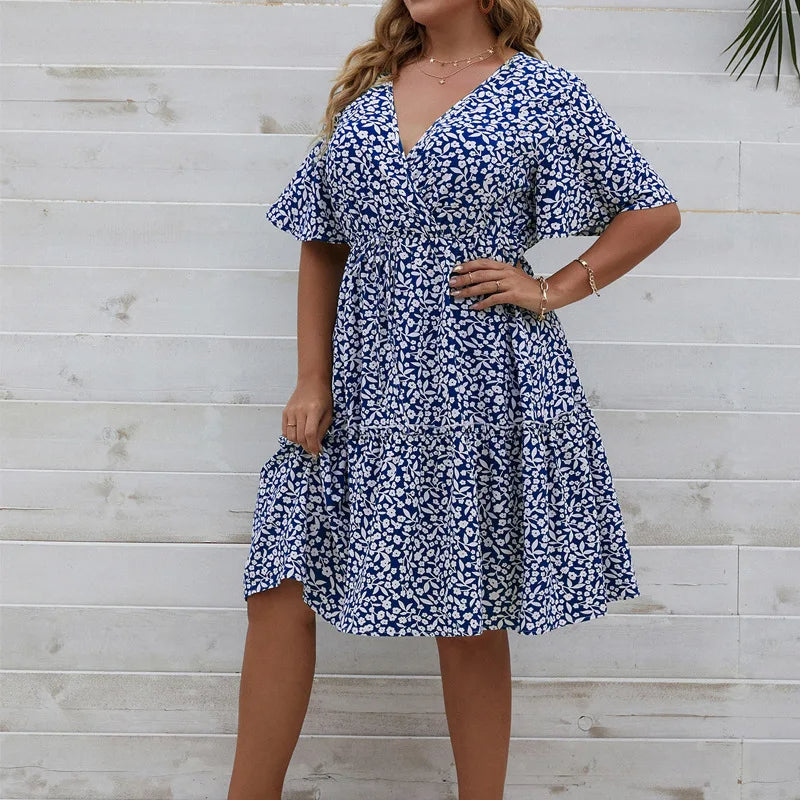 Frau in blau-weißem Sommerkleid mit Blumenmuster vor Holzwand.