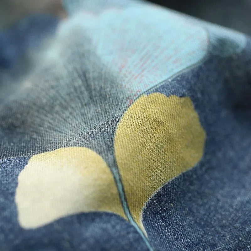 Blauer Jeansstoff mit gelbem und blauem Ginkgo-Blattmuster, Nahaufnahme, Textildesign.