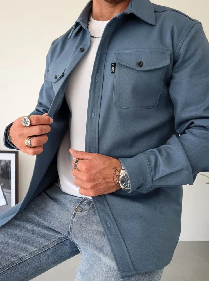 Mann trägt blaue Overshirt-Jacke, weiße T-Shirt, Jeans; modische Herrenbekleidung.