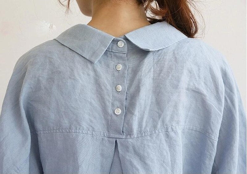 Frau in hellblauer Leinenbluse mit Knopfleiste hinten, elegantes Design, modische Damenbekleidung.