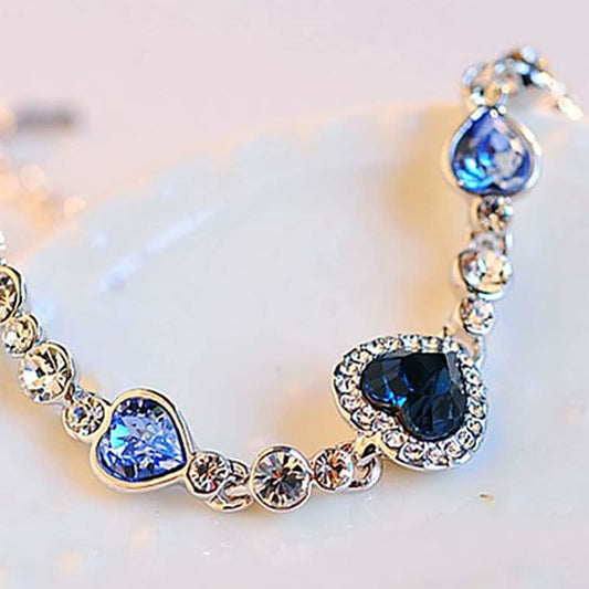 Silbernes Armband mit blauen Herzanhängern und Kristallen, eleganter Schmuck für Damen.