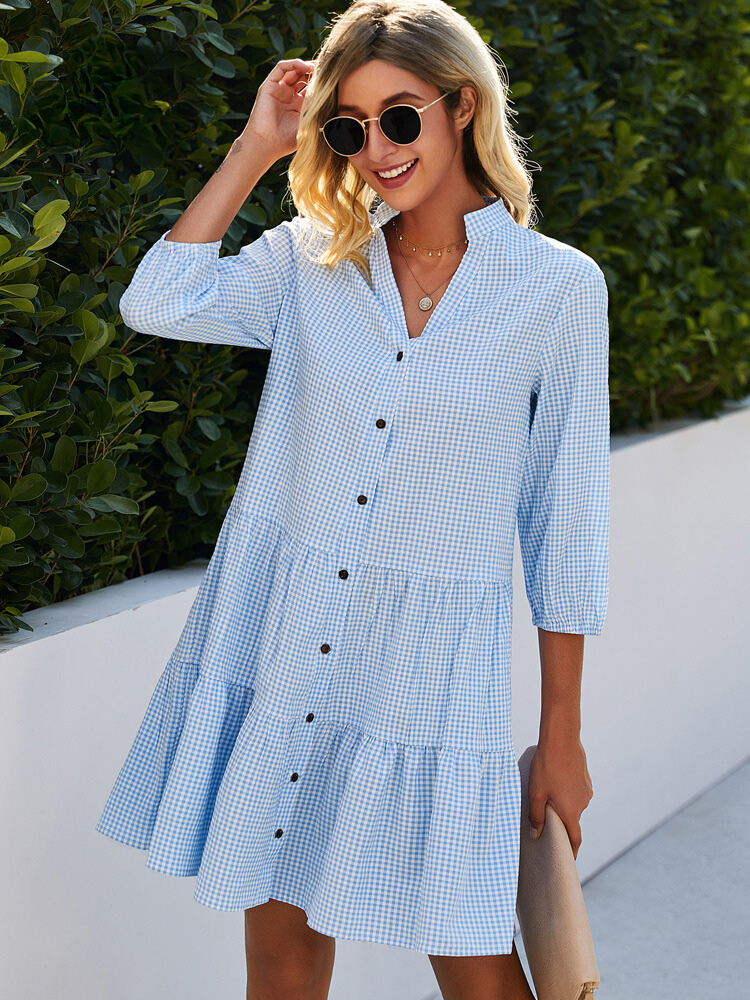 Frau in blau-weiß kariertem Sommerkleid mit Knopfleiste, Sonnenbrille, lächelnd, draußen.