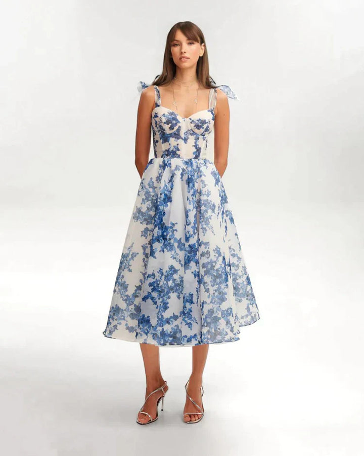 Frau in charmantem blauem Blumenkleid, knielang, mit Spaghettiträgern, elegantes Design.