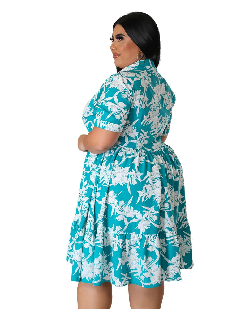 Frau in türkis-weißem Blumenkleid, Plus-Size, Sommermode, Kurzarm, Rückansicht.