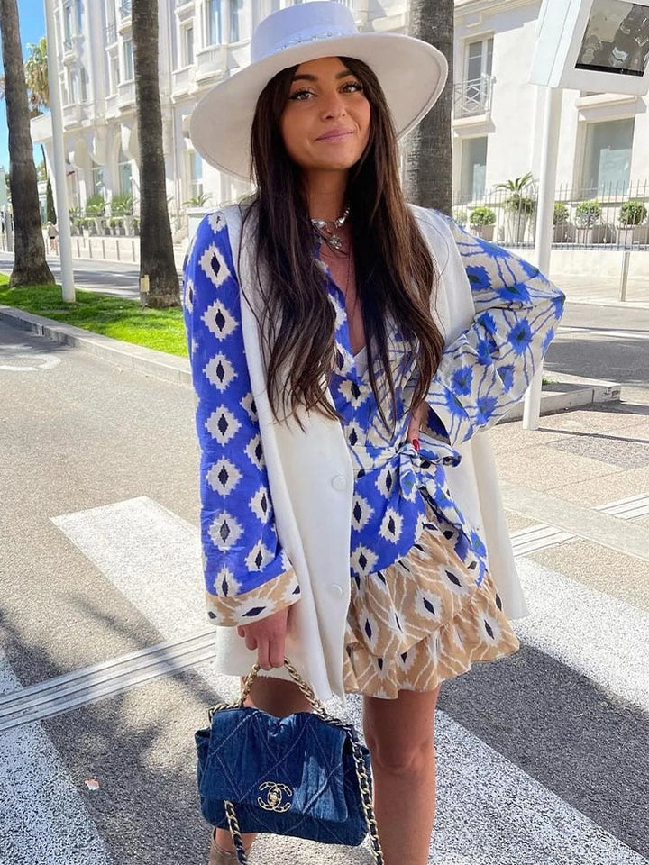 Frau in blau-weißem Kleid mit Hut und Designer-Handtasche auf Straße bei Sonnenschein.