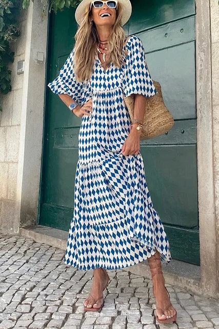 Frau im blau-weiß karierten Sommerkleid, Strohhut, Sandalen, vor grüner Tür.