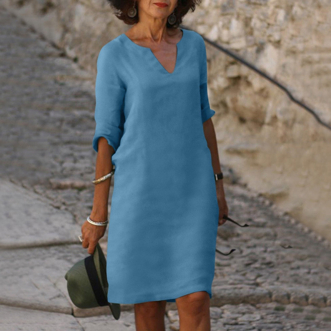 Frau in blauem Leinenkleid auf Kopfsteinpflasterweg, Sommermode, lässiger Stil.