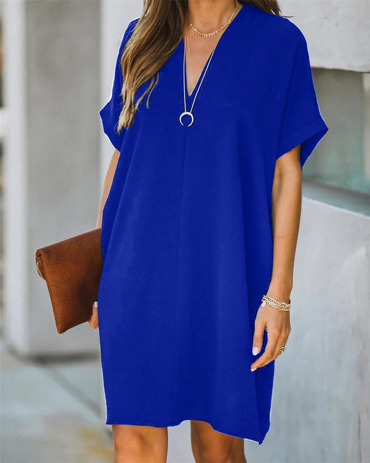 Frau in blauem Sommerkleid mit V-Ausschnitt, braune Clutch, lässiger Stil, modisch.