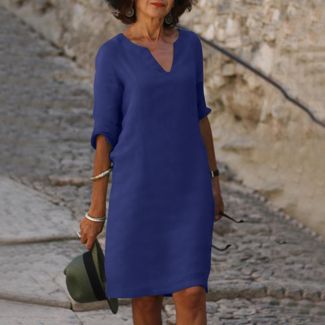 Frau in blauem Sommerkleid, V-Ausschnitt, auf Kopfsteinpflasterweg, modisch, elegant.