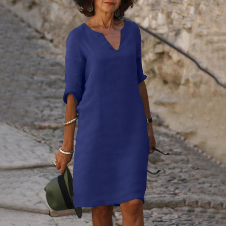 Frau in blauem Sommerkleid, V-Ausschnitt, auf Kopfsteinpflasterweg, modisch, elegant.