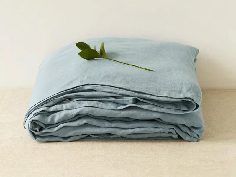 Zusammengefaltete blaue Leinenbettwäsche mit grünem Blatt, hochwertig, nachhaltig, stilvoll.