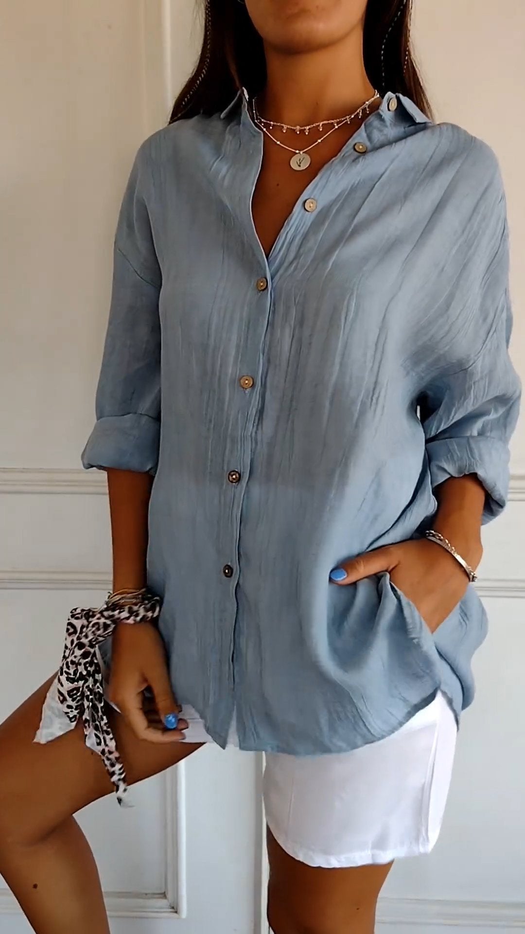 Frau in hellblauer Leinenbluse, weiße Shorts, Schmuck, lässiger Sommerlook.