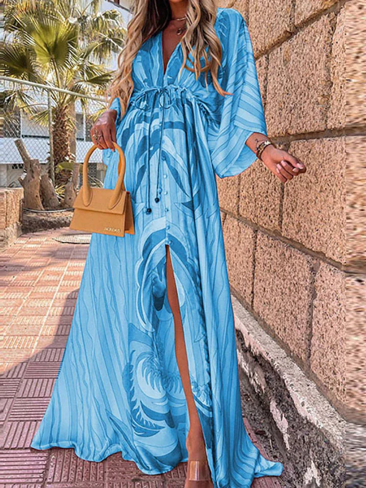 Frau in blauem Maxikleid mit Muster, gelbe Handtasche, Sommermode, draußen, Palmen im Hintergrund.