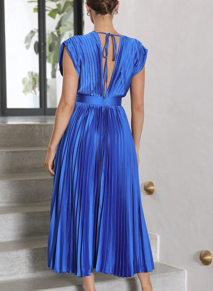 Frau in blauem, plissiertem Kleid mit Rückenausschnitt auf Treppe, elegantes Abendmode-Design.