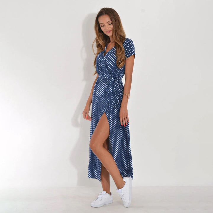 Frau in blauem gepunktetem Sommerkleid mit Schlitz, weiße Sneaker, lässiger Look.