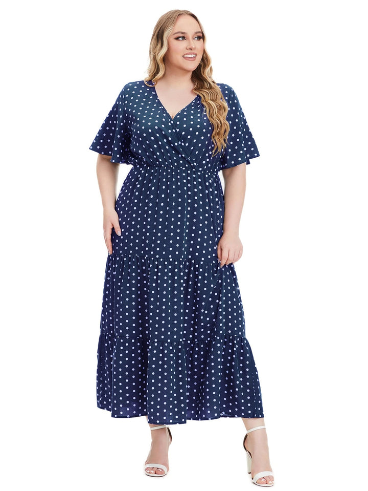 Frau im blauen gepunkteten Maxikleid, V-Ausschnitt, Plus-Size, Sommermode, weiße Sandalen.