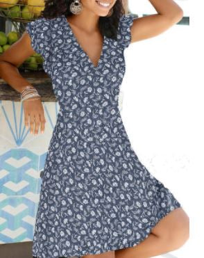 Frau in blauem Sommerkleid mit Blumenmuster, V-Ausschnitt, kurze Ärmel, lächelnd.