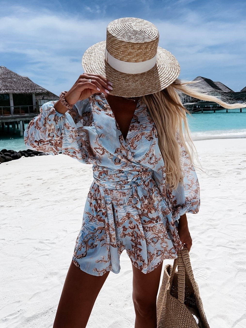 Frau im blauen Sommerkleid mit Strohhut am Strand, tropische Kulisse, Urlaubsmode.
