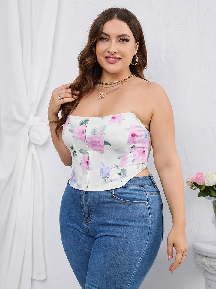 Frau in floralem, schulterfreiem Top und blauer Jeans vor weißem Hintergrund.