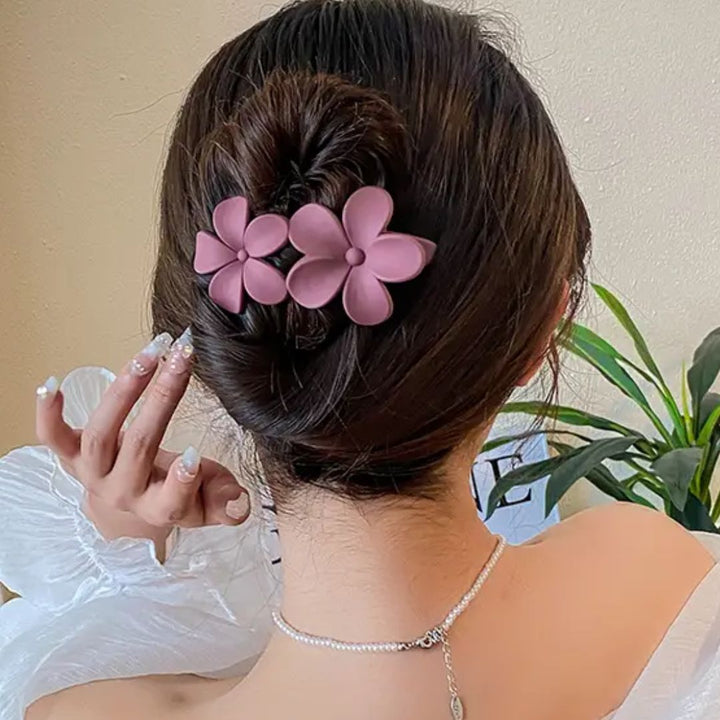 Frau mit rosa Blumen-Haarklammer, eleganter Dutt, weiße Bluse, stilvolle Frisur, Rückansicht.