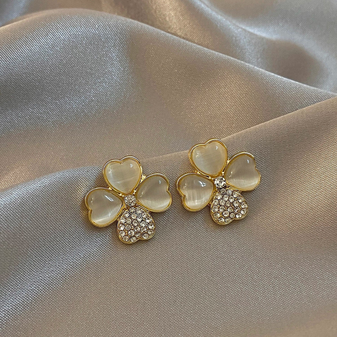 Goldene Kleeblatt-Ohrringe mit Perlmutt und Strasssteinen auf Seidenstoff.