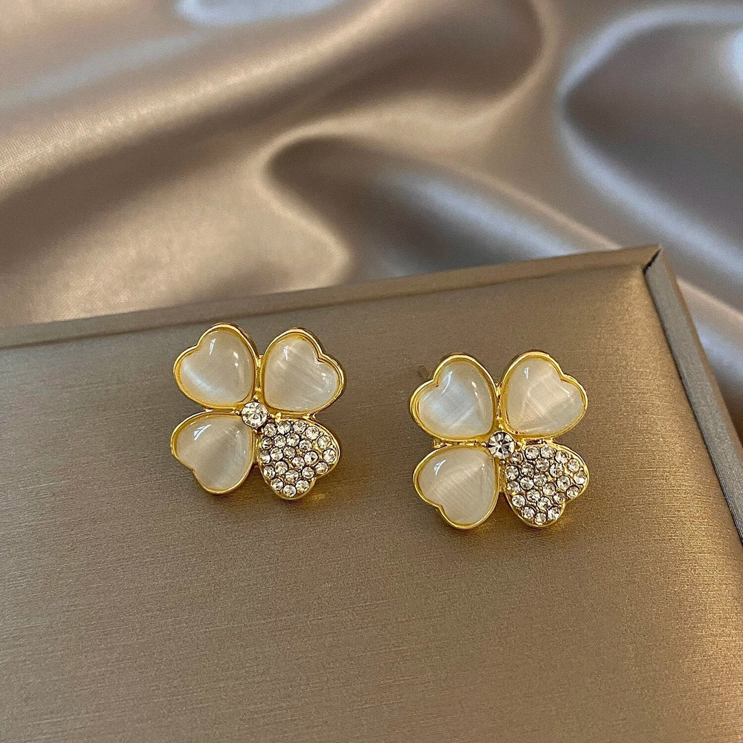 Goldene Ohrringe mit Herzblüten-Design, Perlmutt und Strasssteinen auf Seidenhintergrund.