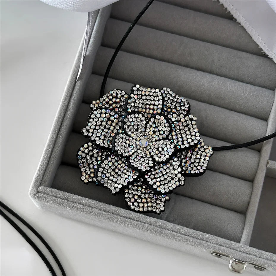Schwarze Blume Halskette mit Strasssteinen in grauer Schmuckschatulle, elegantes Design.
