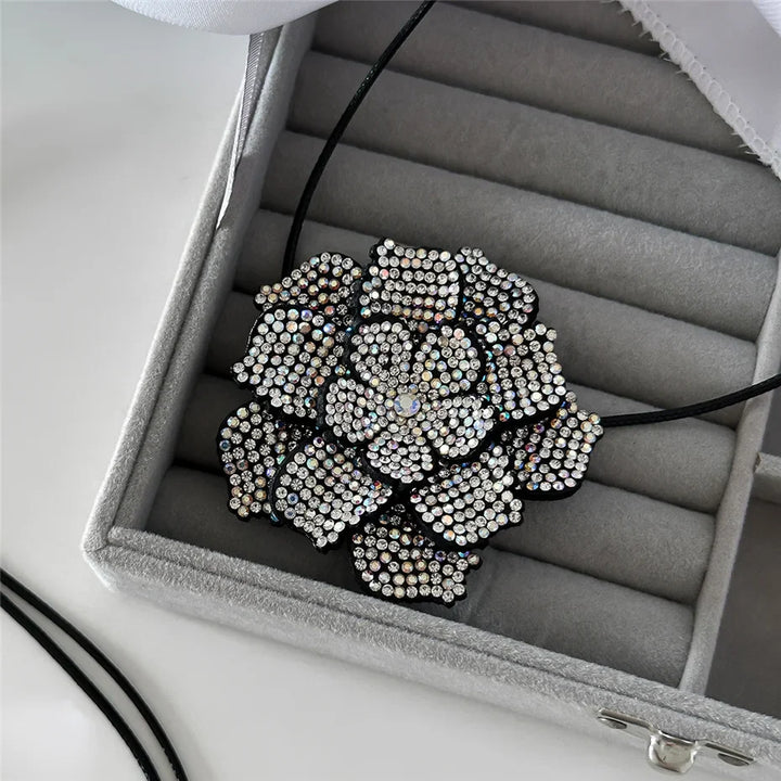 Schwarze Blume Halskette mit Strasssteinen in grauer Schmuckschatulle, elegantes Design.