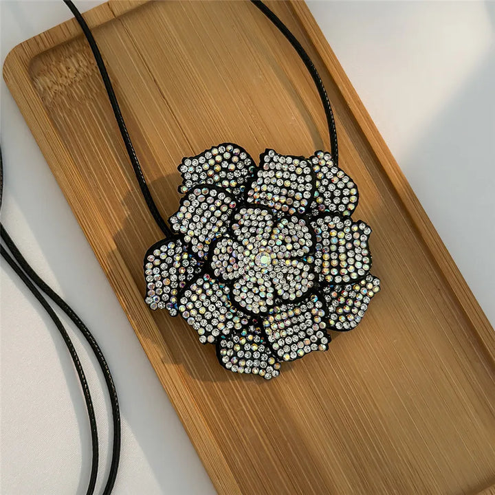 Schwarze Blume Halskette mit Strasssteinen auf Holztablett, eleganter Modeschmuck Accessoire.