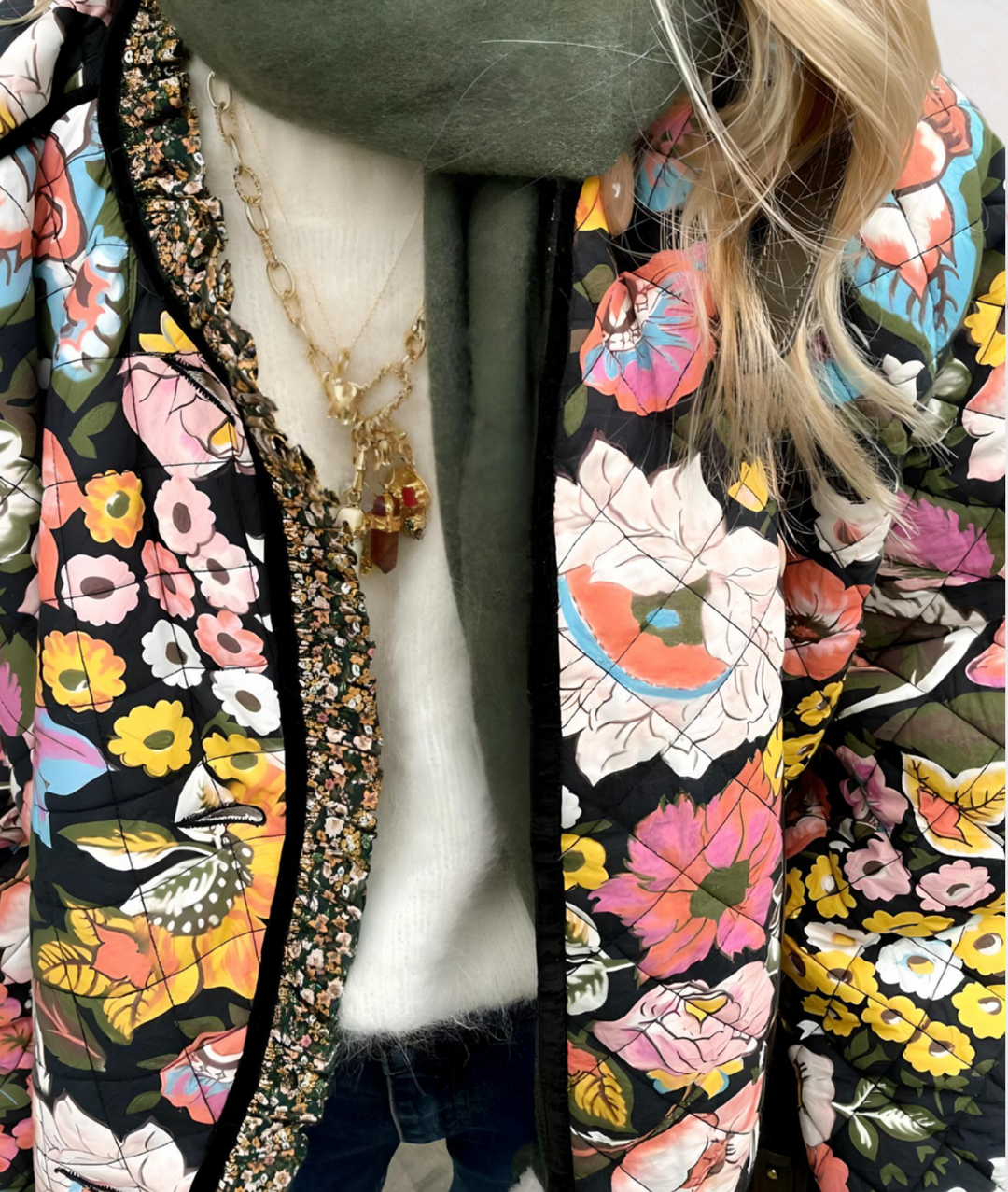 Bunte Damenjacke mit Blumenmuster, gesteppt, über weißem Pullover und grünem Schal.