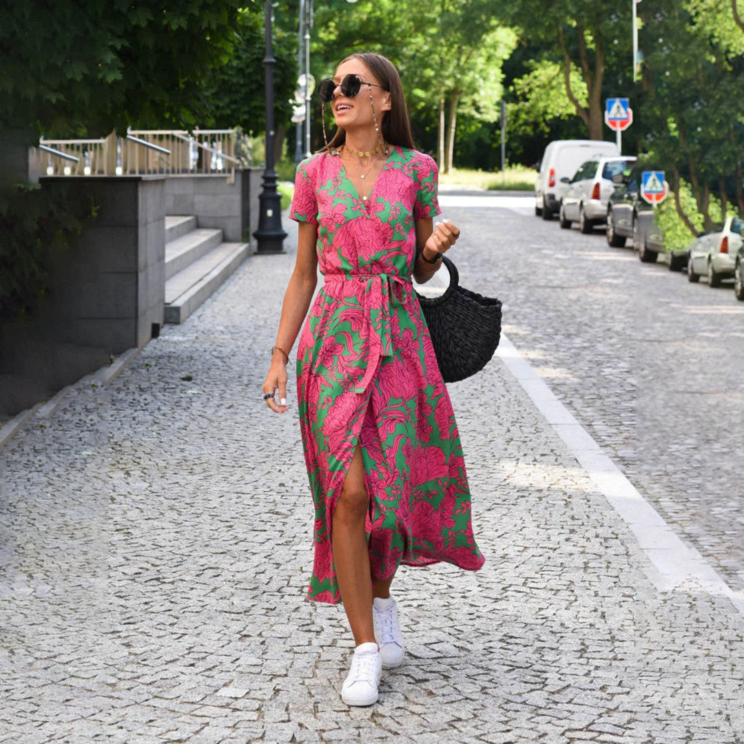 Frau im rosa-grünen Sommerkleid spaziert auf gepflasterter Straße, trägt weiße Sneaker.