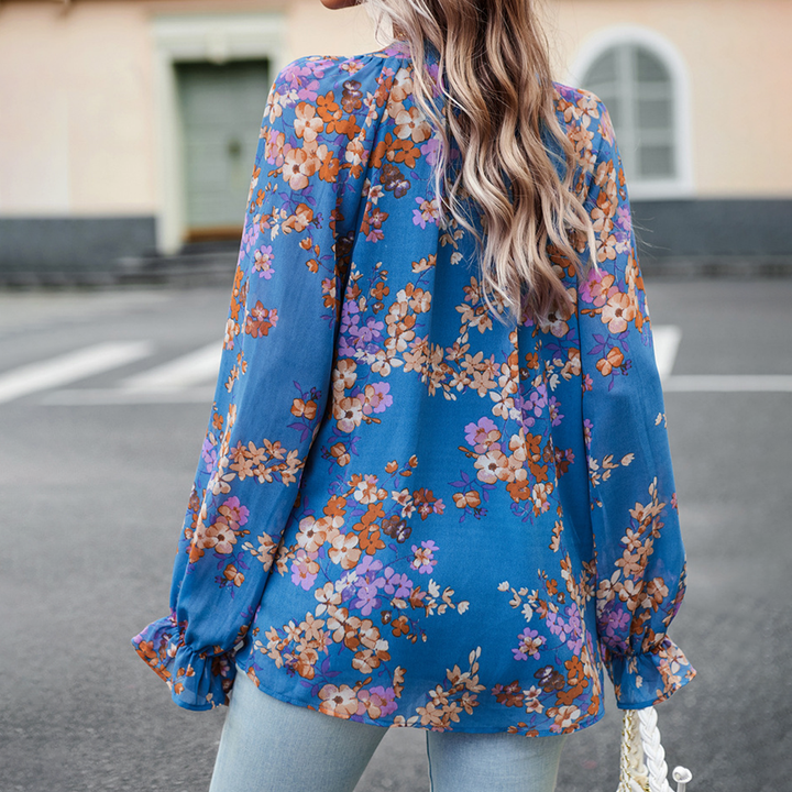 Frau in blauer, geblümter Bluse aus Chiffon, Rückansicht, lässiger Stil, Straße im Hintergrund.
