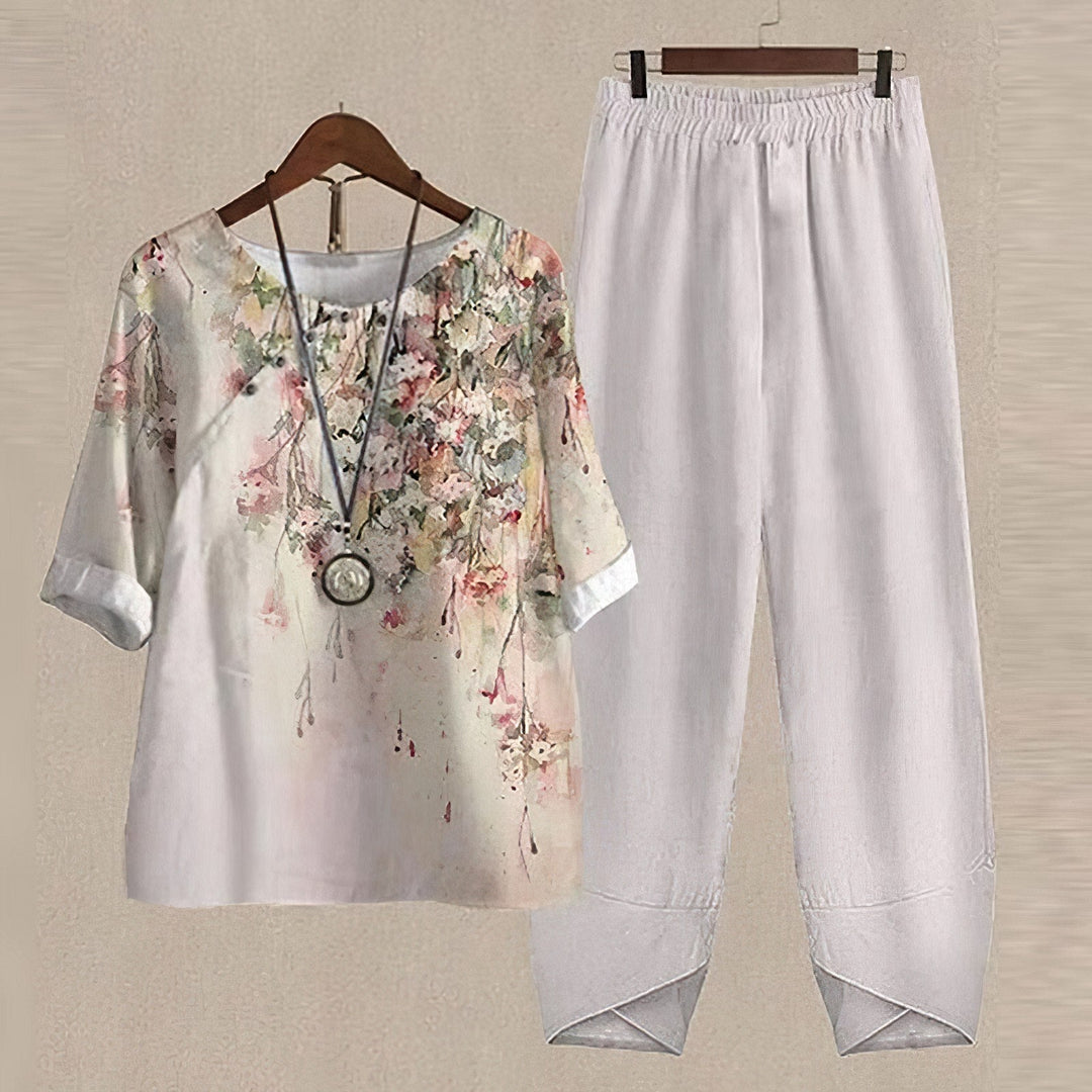 Weiße Damenbluse mit Blumenmuster und weiße Leinenhose auf Kleiderbügel.