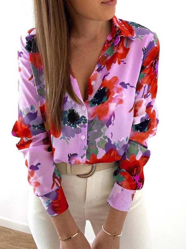 Frau in bunter Blumenbluse, lila und rot, mit weißer Hose, modisch, elegant, Frühlingstrend.