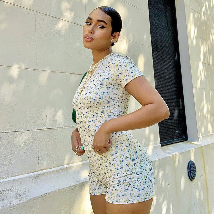 Frau in geblümtem Jumpsuit, weiß-blau, Sommermode, draußen, vor heller Wand.