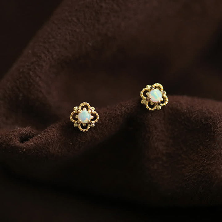 Goldene Ohrringe mit Opal, Blumenform, auf braunem Stoff, eleganter Schmuck, Damenaccessoire.