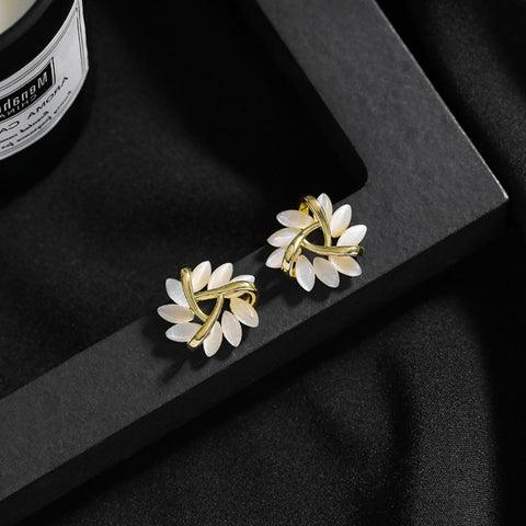 Goldene Ohrringe mit weißen Blütenblättern auf schwarzem Hintergrund, eleganter Schmuck.