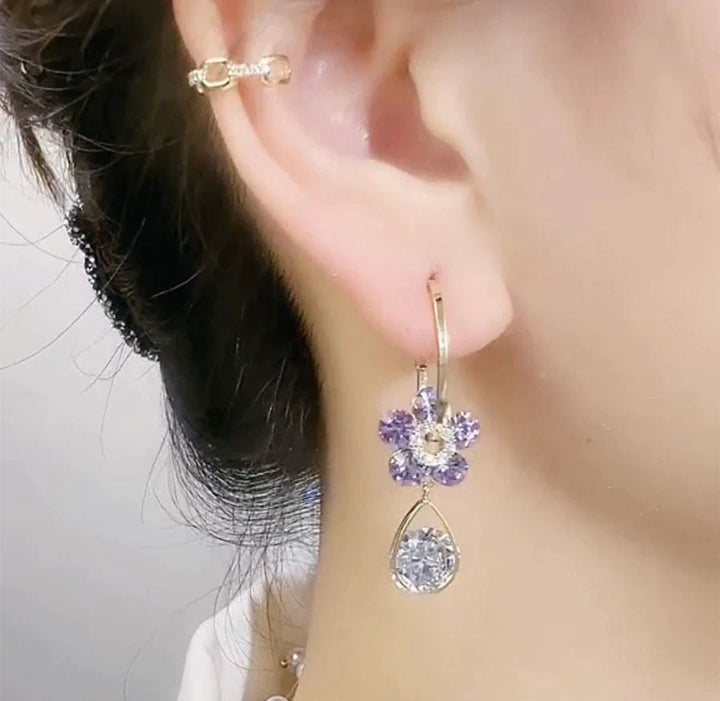 Frau mit lila Blumenohrring und Ohrstecker, eleganter Schmuck, Nahaufnahme.